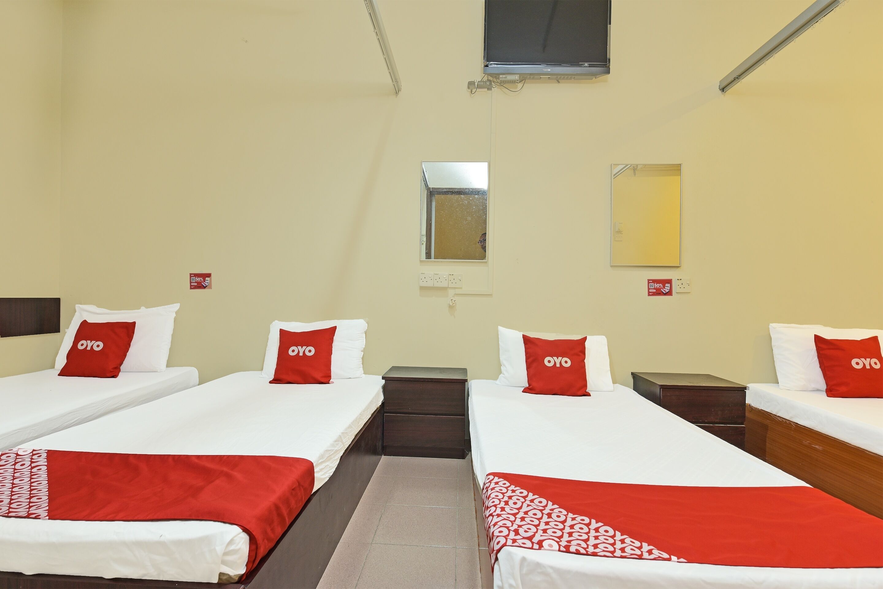 Una habitación de hotel con dos camas, cada una con ropa de cama blanca y almohadas rojas, una mesita de noche pequeña, un espejo y una ventana.