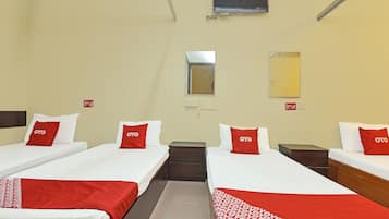 A hotel room with two beds, each with white bedding and red pillows, a small bedside table, a mirror, and a window.