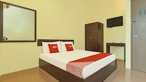 Une chambre d’hôtel avec un grand lit, une armoire, une petite table et un téléviseur fixé au mur.