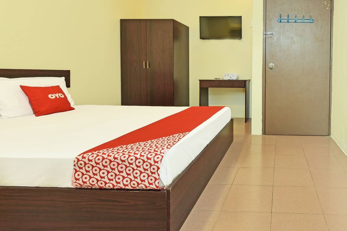 Une chambre d’hôtel avec un lit, une armoire, une petite table avec une horloge et une porte.