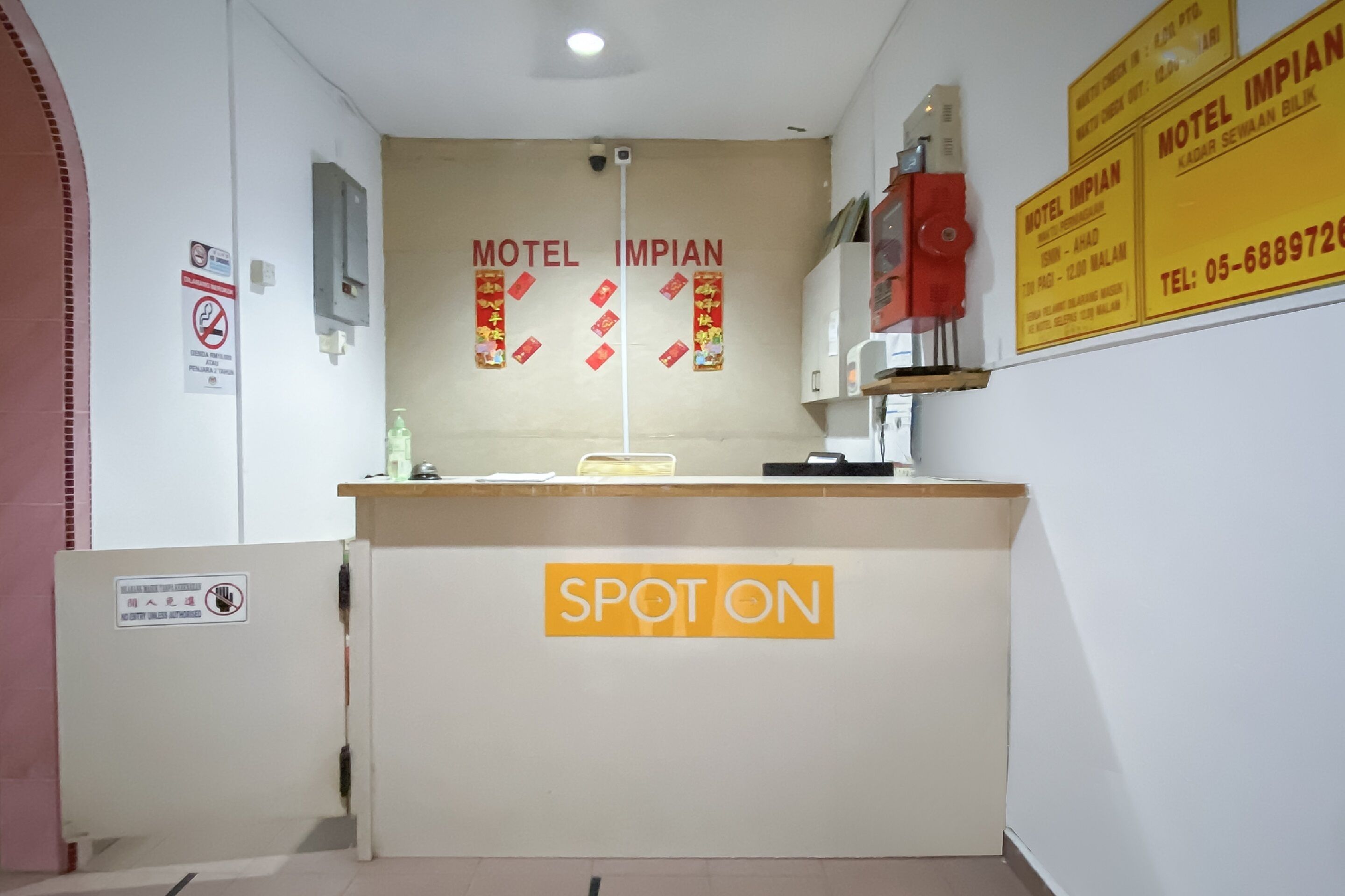 En receptionsdisk med et skilt, der siger "SPOT ON", og en væg med flere skilte for "Motel Impiat" samt et telefonnummer.