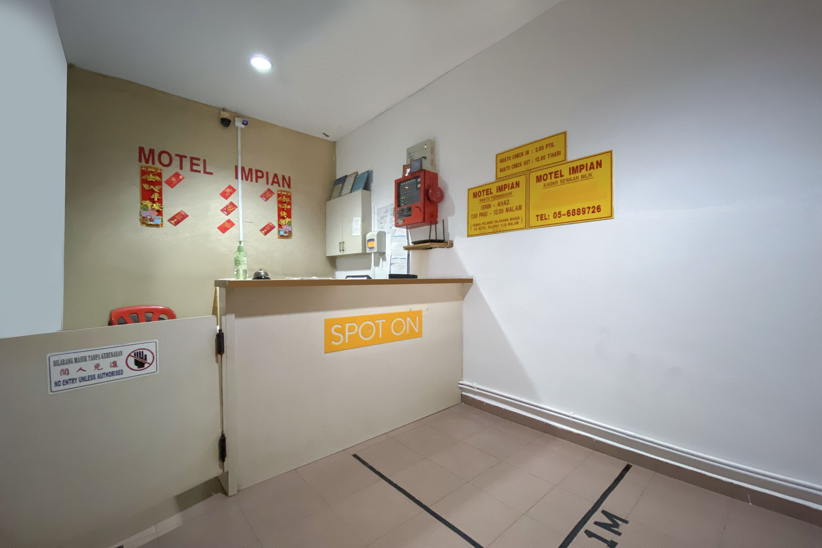 Un espace d’accueil d’hôtel avec un comptoir, une enseigne indiquant « SPOT ON » et plusieurs panneaux pour le « Motel Impiat », avec les coordonnées.