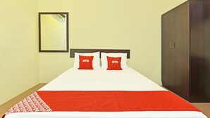 Un lit recouvert d’une couvre-lit rouge et blanche, deux oreillers rouges ornés du mot « OYO », une armoire en bois et un miroir accroché au mur.
