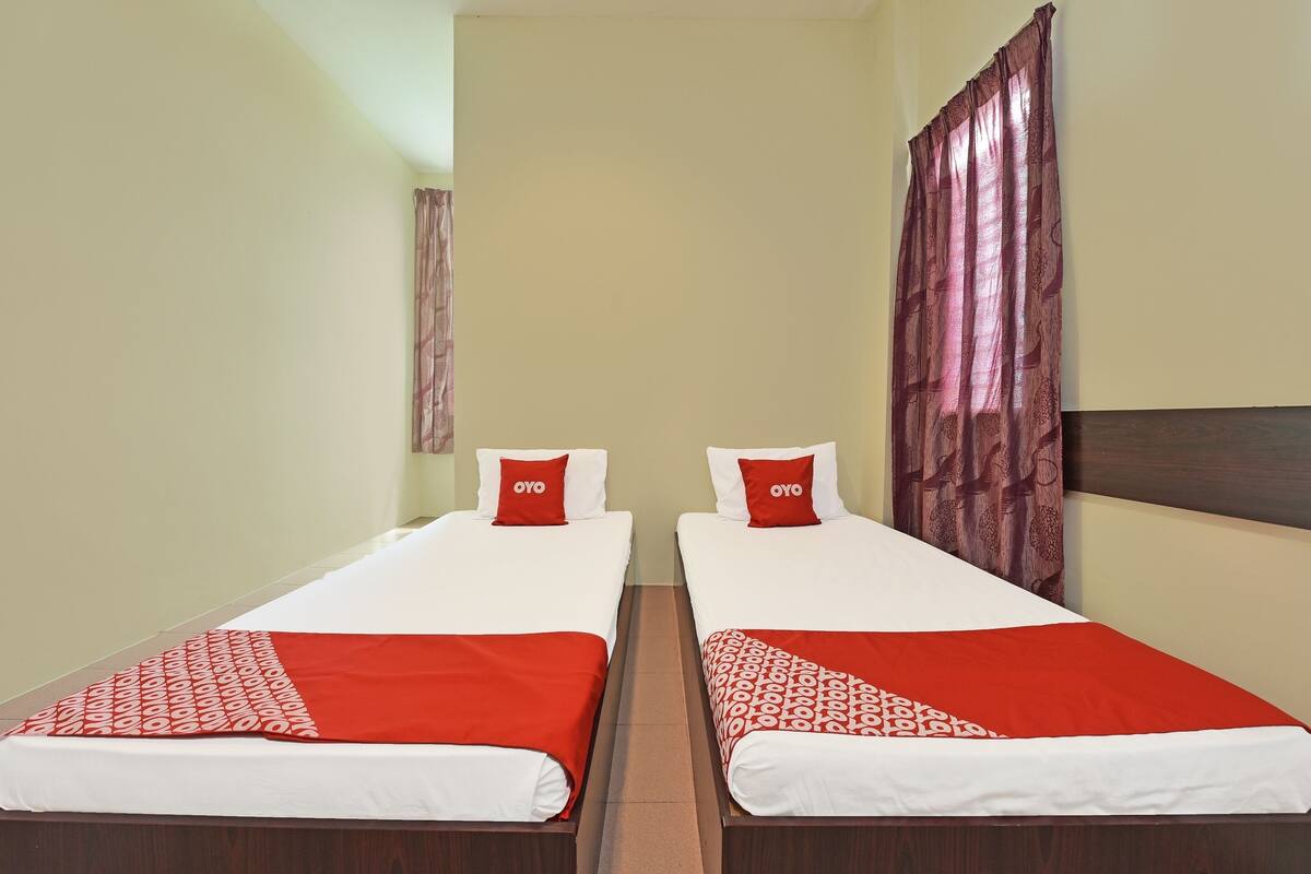 Une chambre d’hôtel avec deux lits simples, chacun recouvert d’une courtepointe rouge et blanche et agrémenté d’oreillers assortis.