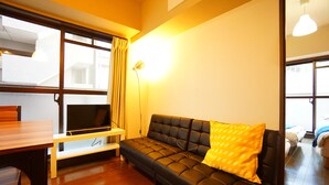 A modern living room with a black leather sofa, a wooden dining table, and a TV on a white stand. - Terry's Apartment Shinsaibashi East I G04C (Osaka)