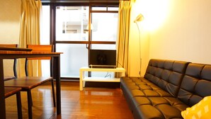 A living room with a sofa, a TV on a stand, a table, and a lamp. - Terry's Apartment Shinsaibashi East I G04C (Osaka)
