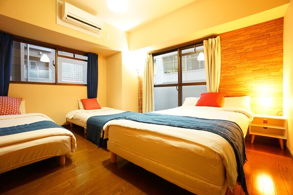 A hotel room with three beds, wooden flooring, a wooden accent wall, and a window with curtains. - Terry's Apartment Shinsaibashi East I G04C (Osaka)