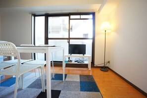 A small room with a white table, two white chairs, a TV on a stand, a floor lamp, and a large window. - Terry's Apartment Shinsaibashi East I G09C (Osaka)