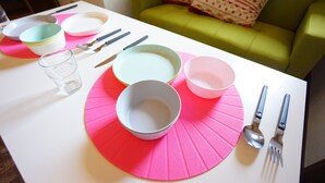 A dining table with plates, bowls, cutlery, and a glass set on pink placemats. - Terry's Apartment Shinsaibashi East I G07B (Osaka)