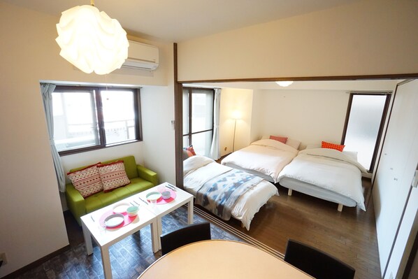 A compact hotel room with a sofa, two beds, a dining table, and a large window. - Terry's Apartment Shinsaibashi East I G07B (Osaka)