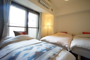 A hotel room with two beds, a window with curtains, a standing lamp, and an air conditioning unit. - Terry's Apartment Shinsaibashi East I G07B (Osaka)
