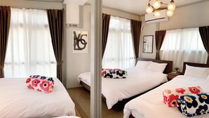 A hotel room with three beds, each with white bedding and floral-patterned pillows. There is a large mirror on one wall, and the room has a modern design with a ceiling light fixture. - Tabisai House (Fukuoka)