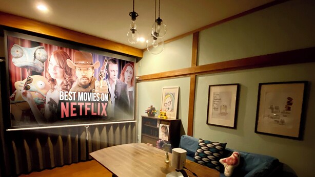 A cozy room with a wooden table, a blue sofa, and a wall with a poster advertising Netflix movies. - Tabisai House (Fukuoka)