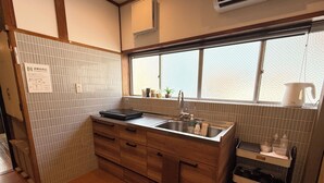 A compact kitchen with a wooden countertop, a sink, and a window above the sink. - Tabisai House (Fukuoka)