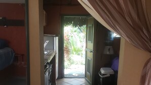 A narrow hallway with tiled flooring leading to a door with a view of greenery outside.