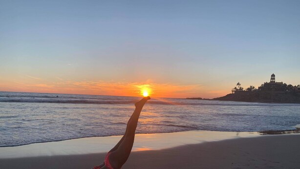 A sunset view from a beach with a person doing a handstand.