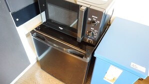 Une cuisine avec un four et un micro-ondes noirs, un réfrigérateur bleu et un plancher en bois.
