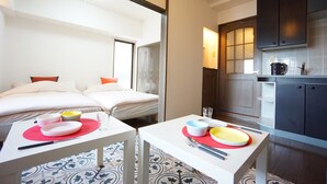 Une chambre d’hôtel comprenant un lit, une table à manger avec des assiettes et des couverts, un coin cuisine avec des placards et un sol à motifs.