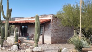 A small brick building with a red-tiled roof, surrounded by cacti and desert plants.