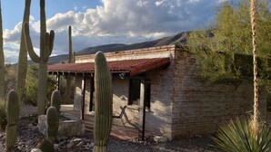 A rustic building with a red-tiled roof, surrounded by cacti and a mountainous backdrop.