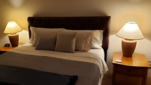A neatly made bed with a dark headboard, two bedside tables with lamps, and a small nightstand with a clock.