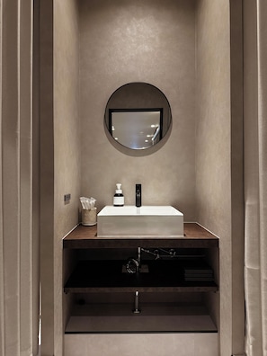 A modern bathroom with a rectangular sink, a round mirror, and a towel dispenser. - TABISAI Luxe (Fukuoka)