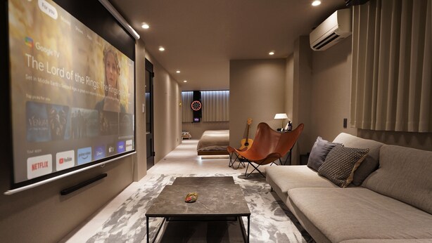 A modern living room with a large screen displaying a movie, a sofa, a coffee table, and a guitar. - TABISAI Luxe (Fukuoka)