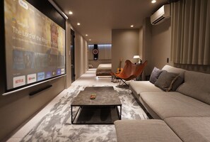 A modern living room with a large screen displaying a movie, a sofa, a coffee table, and a guitar. - TABISAI Luxe (Fukuoka)