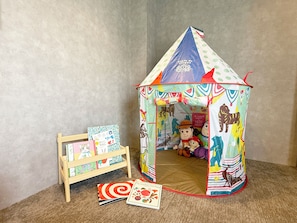 Une tente de jeu aux motifs colorés, un petit présentoir en bois avec des livres et une carte posée sur le sol.