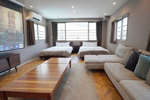 Une chambre d’hôtel avec deux lits, un canapé, une table en bois et un grand écran de télévision.