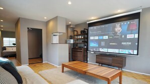 Un salon moderne avec un grand téléviseur à écran plat fixé au mur, une table basse en bois et un canapé gris.