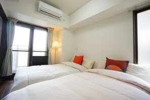 A hotel room with two beds, a window with curtains, an air conditioning unit, and a lamp. - Terry's Apartment Shinsaibashi East I G13B (Osaka)