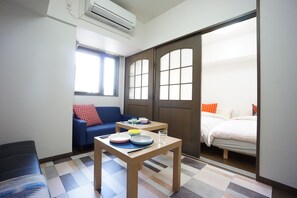 A compact hotel room with a sofa, a small table with plates and a glass, a bed, and a sliding door leading to another room. - Terry's Apartment Shinsaibashi East I G13B (Osaka)