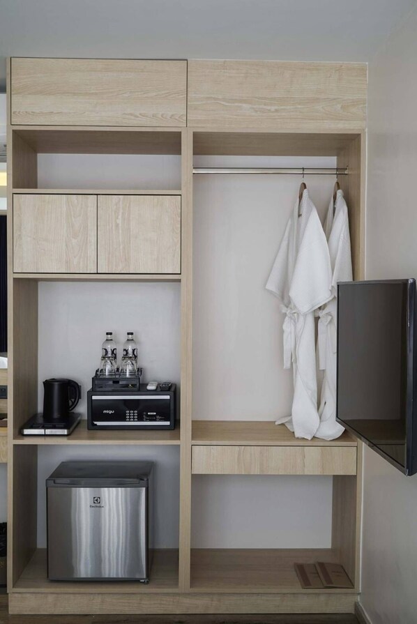 A modern hotel room with a wooden wardrobe, a minibar, a coffee machine, a mini-fridge, and a TV. - NORN Boutique Hotel (Chiang Mai)
