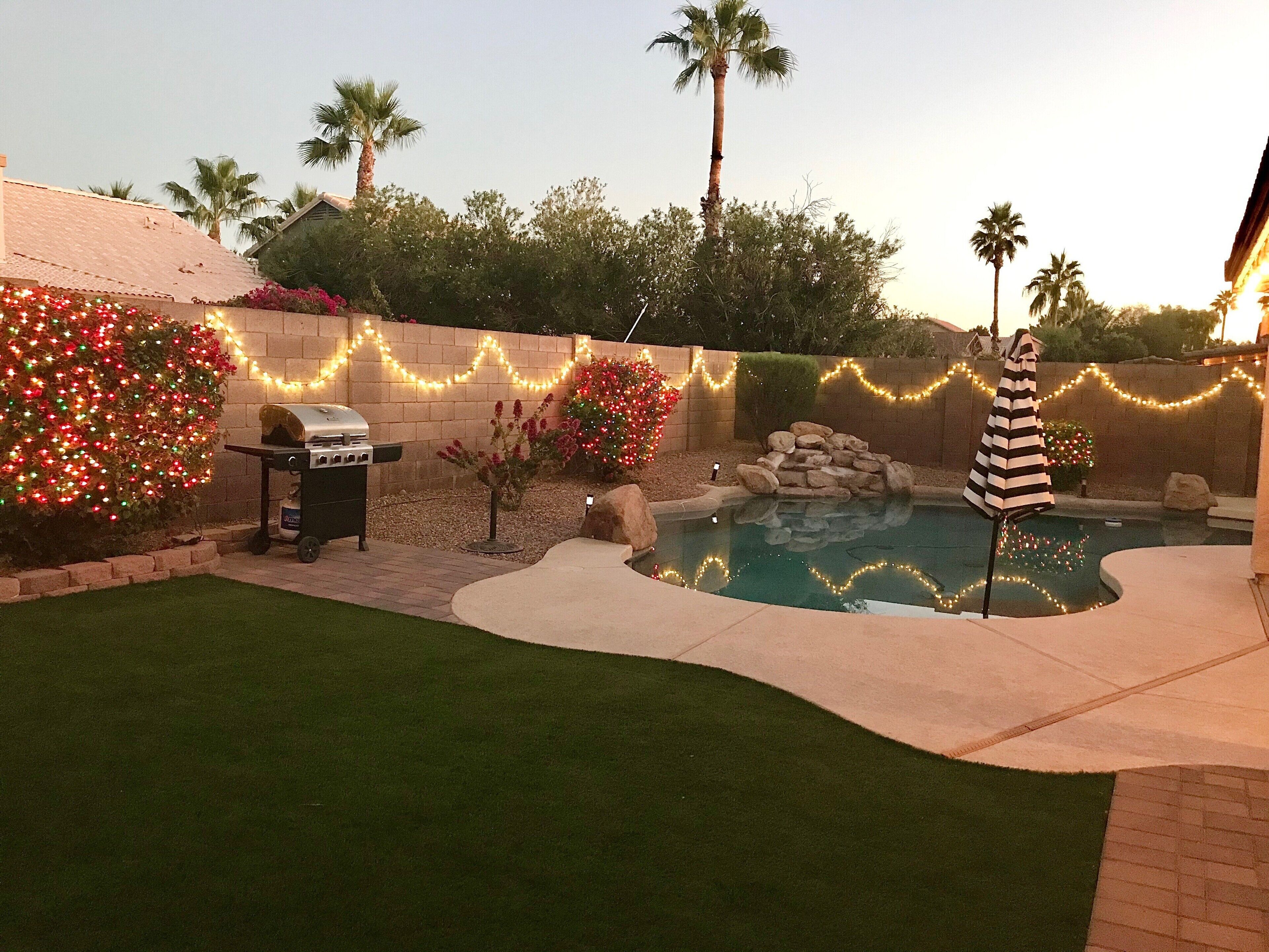Un patio trasero con piscina, parrilla y luces decorativas.