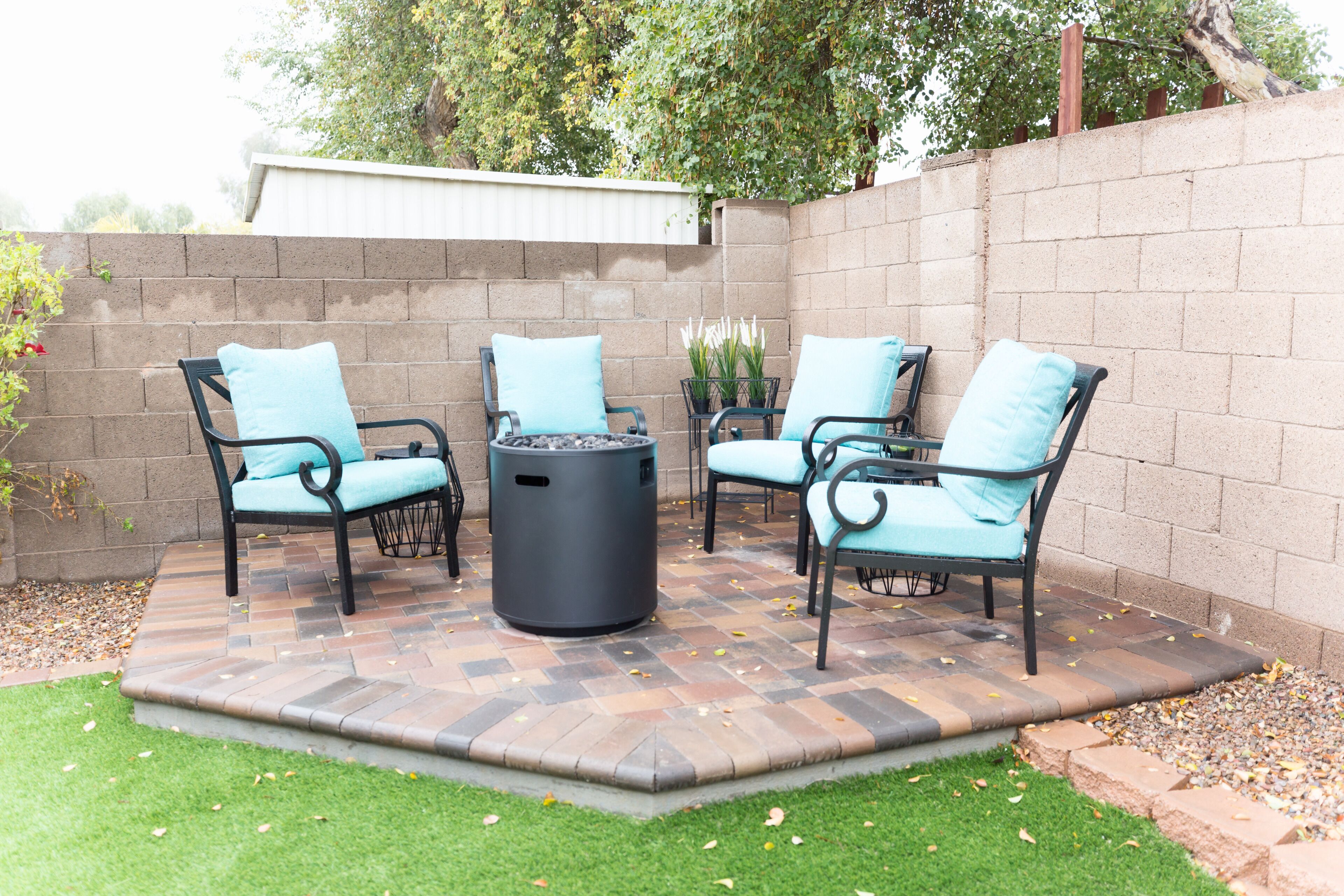 An outdoor patio with four chairs and a table, surrounded by a brick wall and a small garden area.