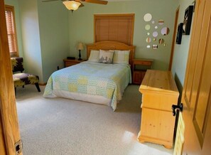 Ein Schlafzimmer mit einem Bett, einem Nachttisch, einem Sessel, einer hölzernen Kommode und einem Deckenventilator.