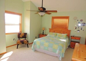 A bedroom with a bed, a chair, a nightstand, a lamp, a ceiling fan, and a window.