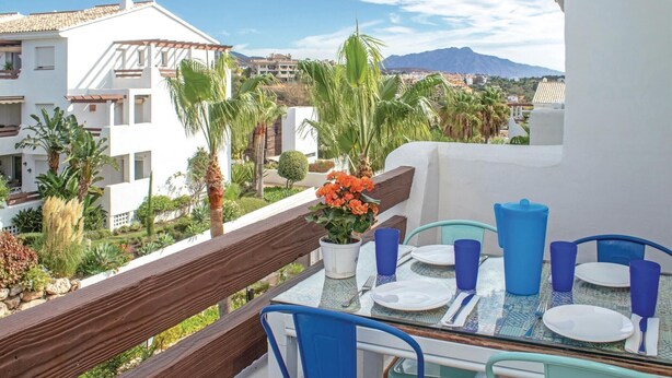 A balcony with a table set for dining, overlooking a residential area with palm trees and houses. - Awesome apartment in Estepona with WiFi (Estepona)