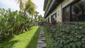 A pathway leading to a building with a stone-tiled entrance, surrounded by lush greenery and tropical plants.