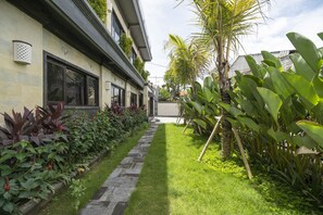 Un giardino curato con un vialetto in pietra, verde rigoglioso e un edificio con ampie finestre e un balcone.