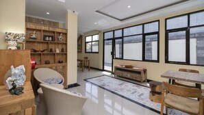A spacious room with a large window, a wooden bookshelf, a dining area with a table and chairs, and a decorative rug.