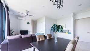 A modern living room with a sofa, dining table, and chairs. There is a large plant on the table, a ceiling fan, and a kitchen area in the background. - Dream City By Himmel (Seri Kembangan)