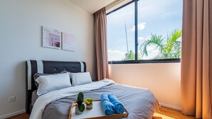 A neatly made bed with a tray of towels and a small plant, a large window with curtains, and two wall art pieces. - Dream City By Himmel (Seri Kembangan)