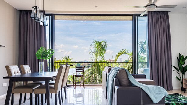 A modern living room with a dining area, large windows, and a balcony with a view of palm trees. - Dream City By Himmel (Seri Kembangan)