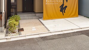 Un bâtiment moderne orné d’une banderole jaune sur laquelle figurent des caractères japonais et le texte « Maison d’hôtes Rakuchou Hanare ».