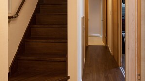 Un escalier en bois menant à un palier, un couloir au plancher en bois et une porte au bout.