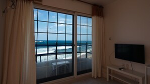 Habitación con ventana grande que ofrece vista al océano, televisión y una pequeña banca blanca.