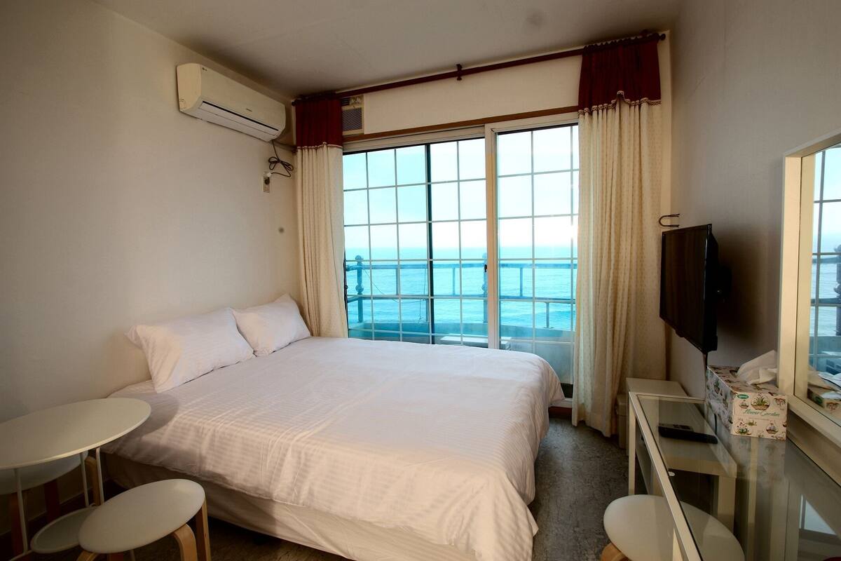 Een hotelkamer met een groot bed, een televisie, een tafeltje en een raam met uitzicht op zee.