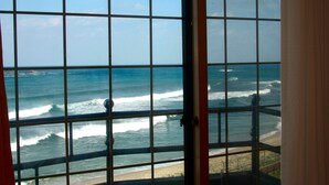 Vista a través de una ventana con diseño de cuadrícula, con vista al océano y una playa arenosa.